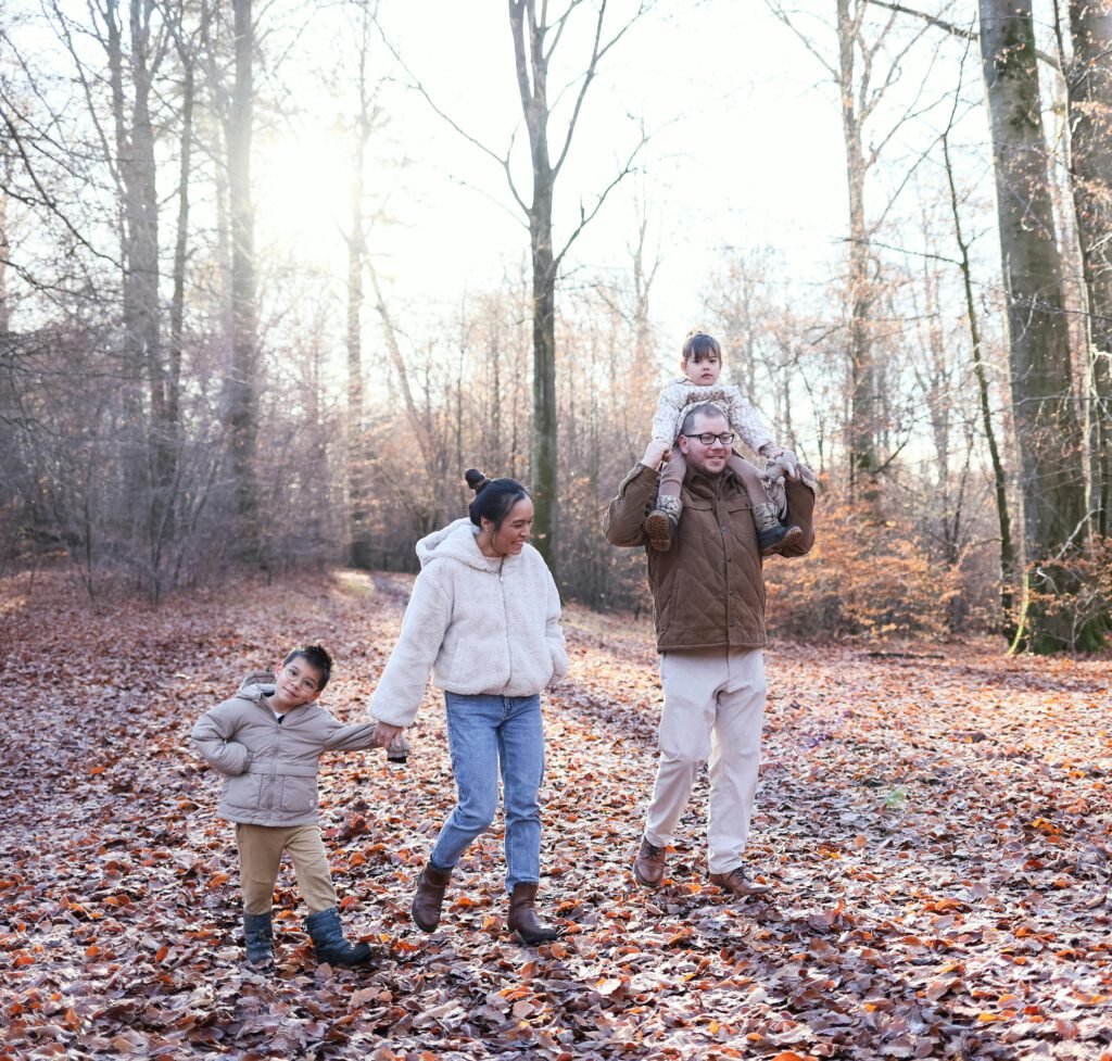 pexels photo 35688928 35688928 Happy family walking through a sunlit autumn forest path, enjoying quality time outdoors.